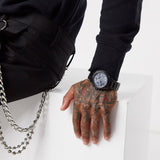 Man's arm with watch, tattooed hand, and black clothing.