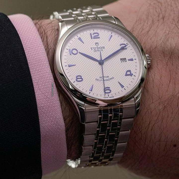 Silver wristwatch on a wrist with a pink shirt sleeve.