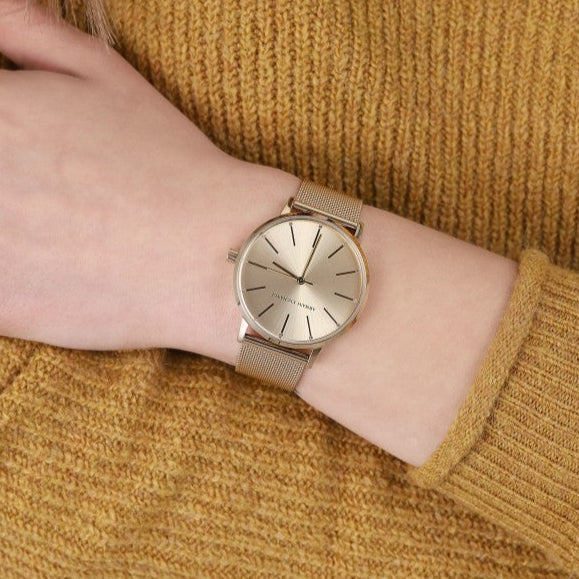 Woman's wrist with gold watch and yellow sweater.