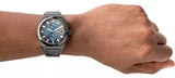 Man's wrist wearing a grey chronograph watch.