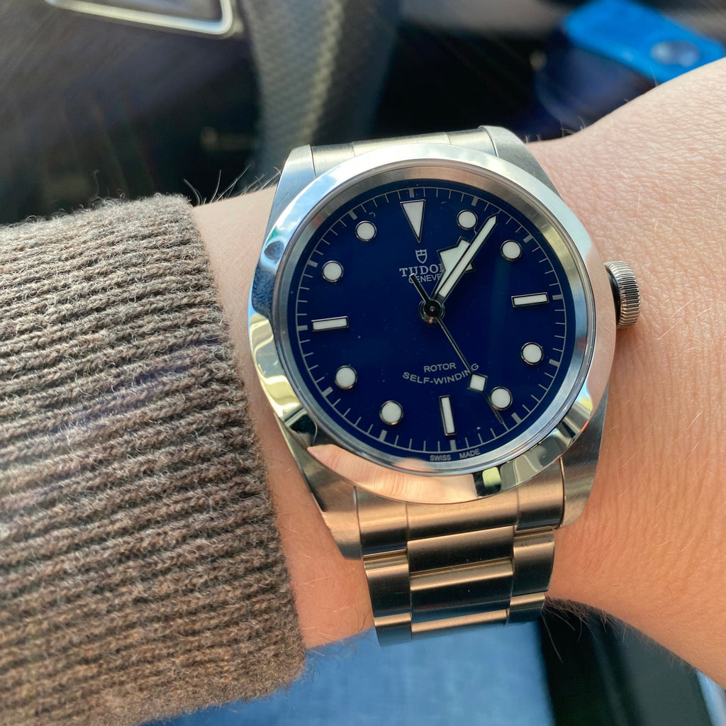 Wrist with a silver watch with a blue face.