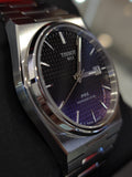 Close-up of a silver Tissot watch with a dark patterned face.