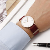 Wrist wearing a watch with a burgundy strap.