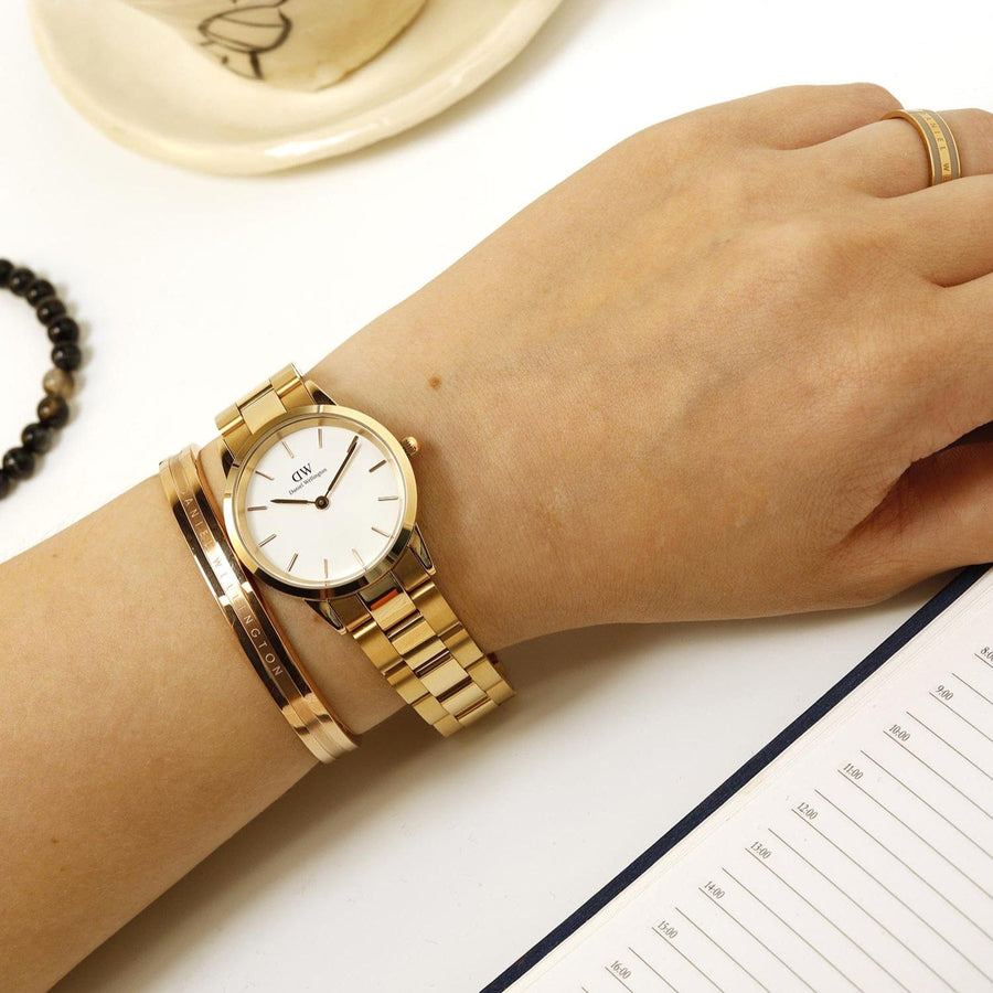 Woman's wrist with gold watch and bracelet, with a ring and notepad.