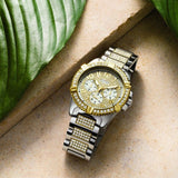 Gold and silver wristwatch on a textured surface with foliage.