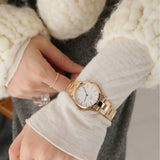 Woman's arm wearing a gold watch and ring.