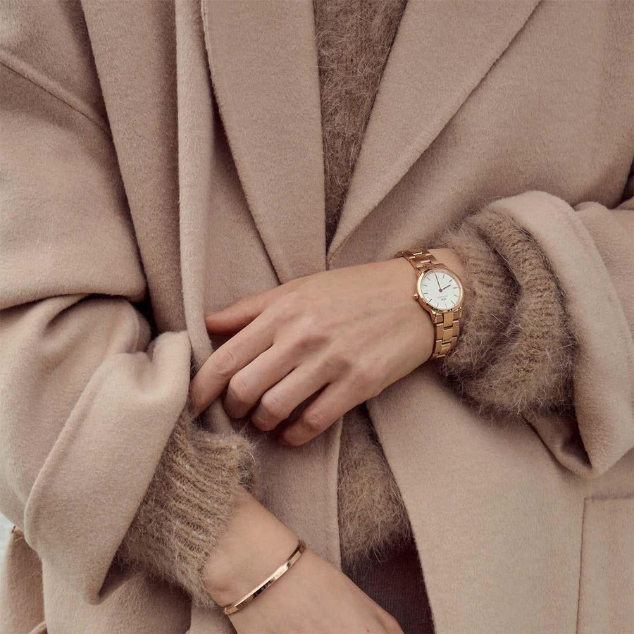 Woman wearing gold watch & bracelet, neutral outfit