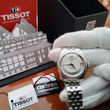 Silver Tissot watch on a gloved hand, with box and tags.