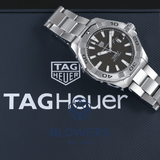 Silver wristwatch on a black surface with the Tag Heuer logo.