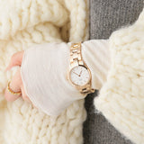 Woman's wrist with gold watch, white sweater, and ring.