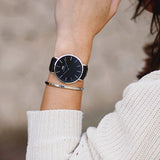 Wrist with black watch and silver bracelet.