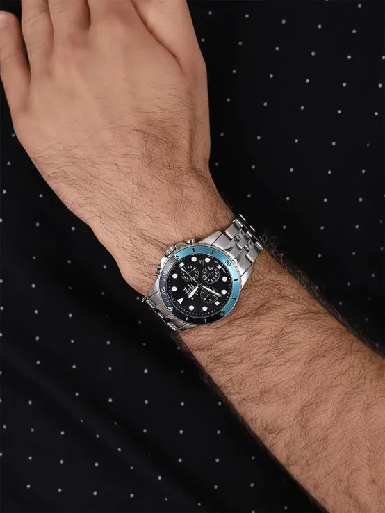 Men's watch detail, silver band, black face with blue accent.