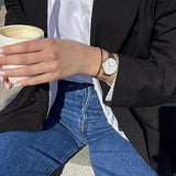 Woman in denim holding coffee, wearing watch and blazer